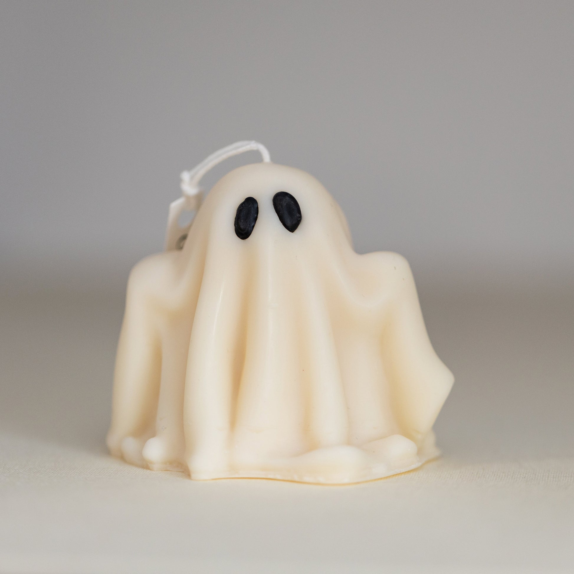 A beige sculptural candle designed to resemble a ghost, with a hanging loop on top.