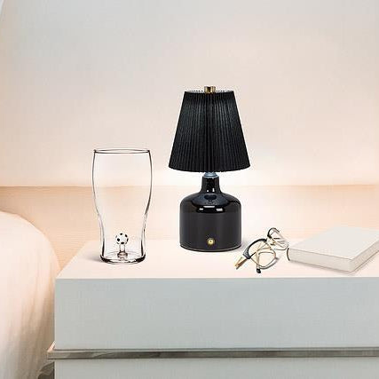 Black table lamp on a white nightstand next to a glass and a book.