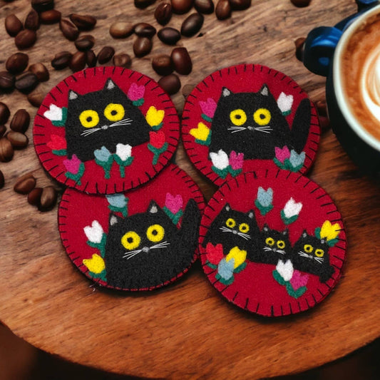 Four red coasters with black cat designs on a wooden surface with coffee beans and a cup of coffee.
