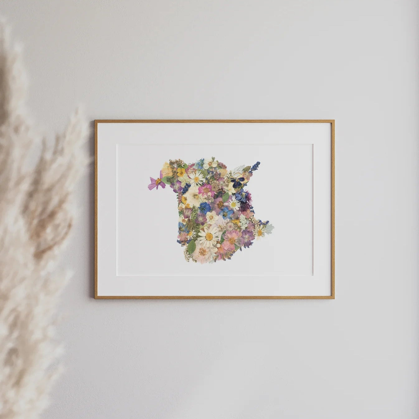 Framed floral art print depicting the shape of New Brunswick on a white wall with pampas grass to the left.