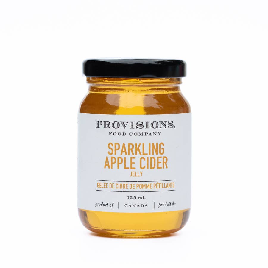 A glass jar of sparkling apple cider jelly with a white label that has the product name and branding, plus a black lid.