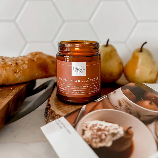 Candle lon a table with bread, pears, and a magazine.