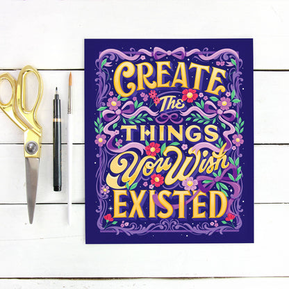 Motivational poster with 'Create the things you wish existed' text on a white wooden surface with scissors and a pen.