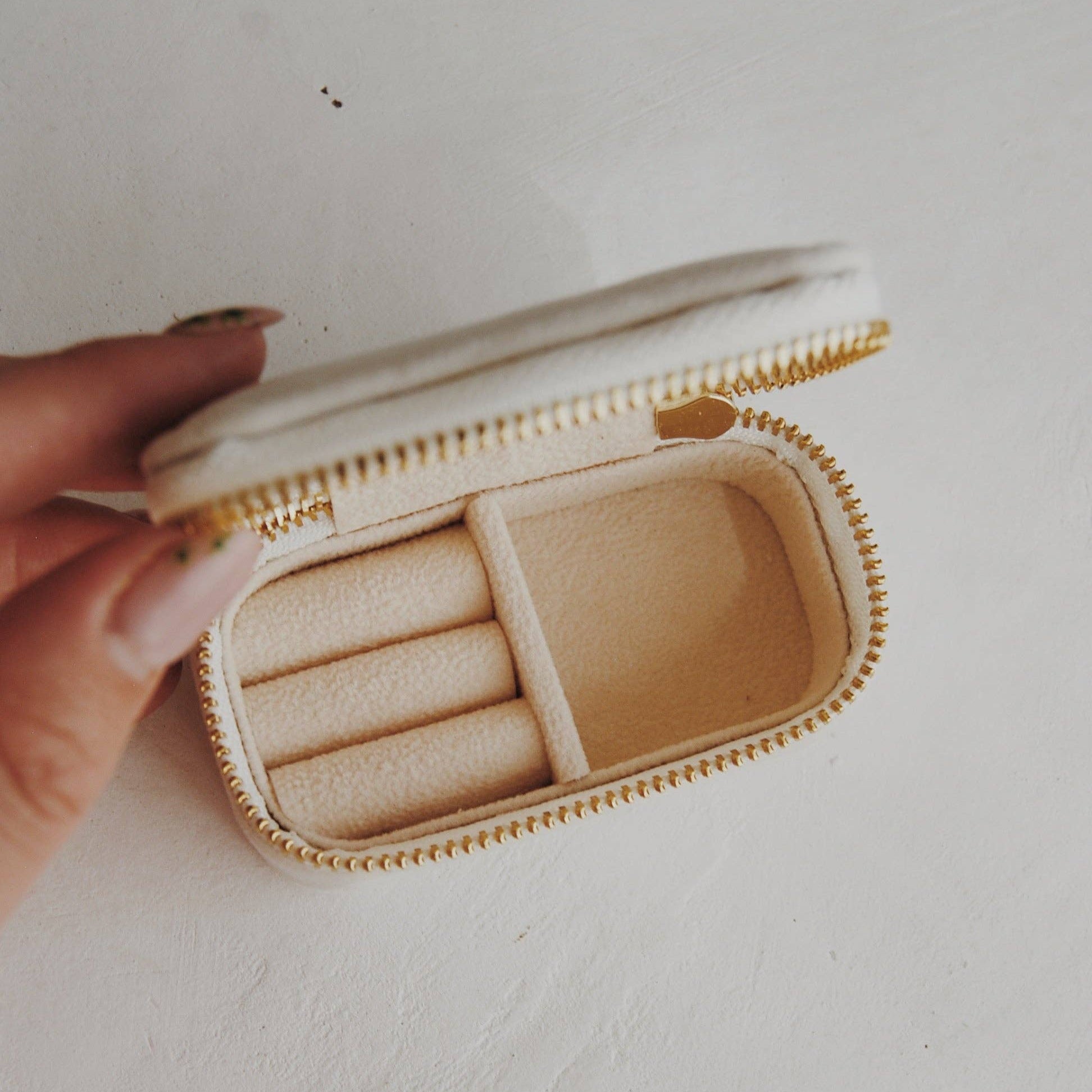 Beige, velvet,  travel jewelry box with a hand holding it on a light background
