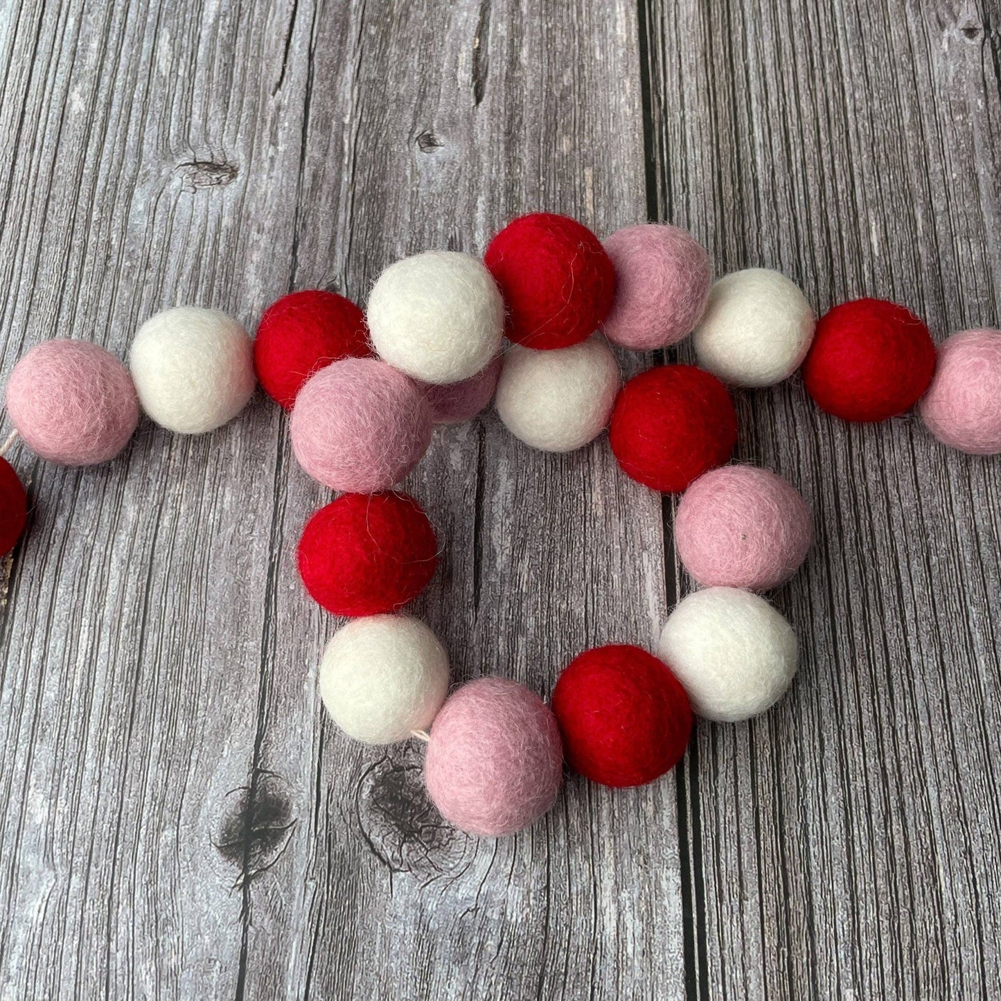 Felt ball garland in red, pink, and white on a wooden surface