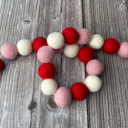 Felt ball garland in red, pink, and white on a wooden surface