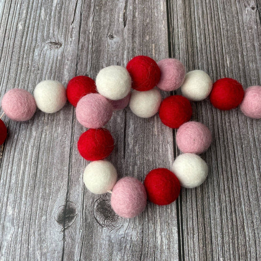 Felt ball garland in red, pink, and white on a wooden surface