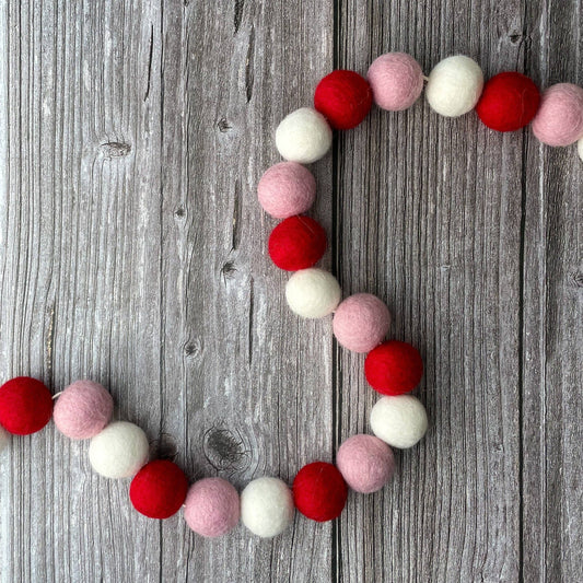 Felt ball garland in red, pink, and white on a wooden surface