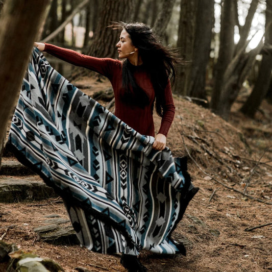 Woman holding a large patterned Mini Tipi blanket in a forest setting