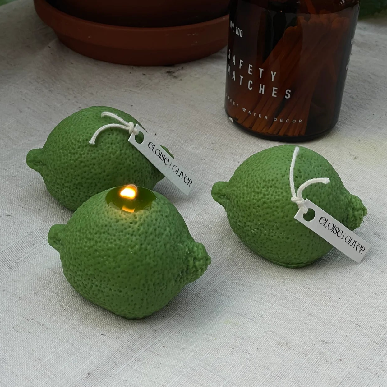 Two green lime-shaped candles with a lit candle and a bottle of alcohol on a white surface.