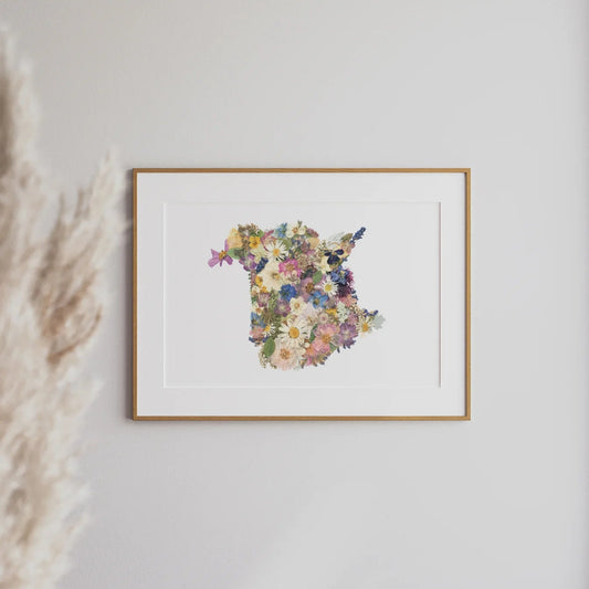 Framed floral art print depicting the shape of New Brunswick on a white wall with pampas grass to the left.
