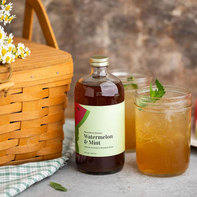 Bottle of watermelon and mint syrup next to a glass of iced tea with a picnic setup.