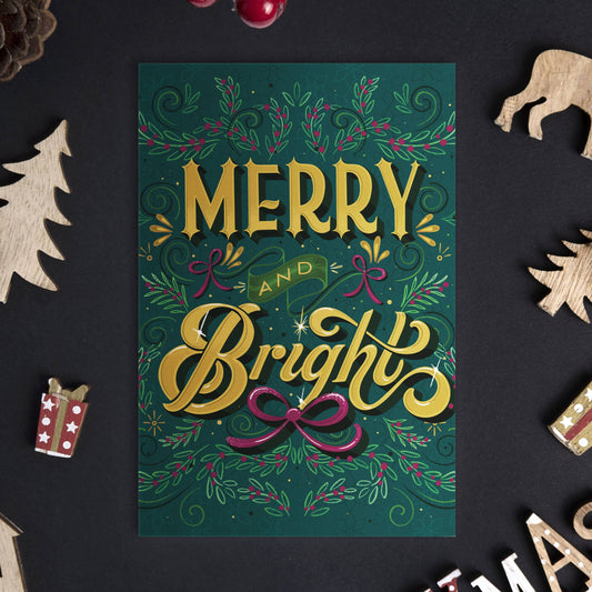 Christmas card with 'Merry and Bright' text surrounded by festive decorations on a dark surface.