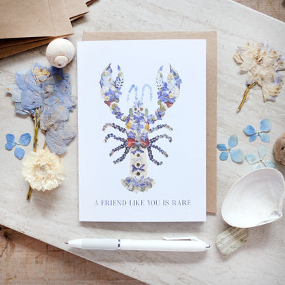 Greeting card with floral lobster design and text on a wooden surface with decorative elements.