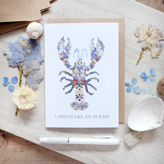Greeting card with floral lobster design and text on a wooden surface with decorative elements.